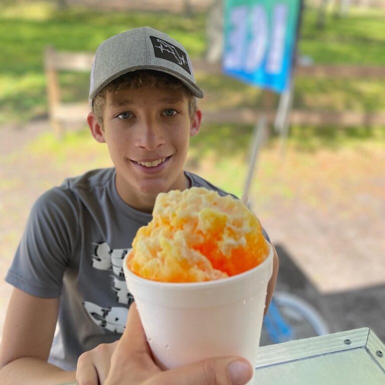 Brandon Jr being handed an orange shaved ice cup.