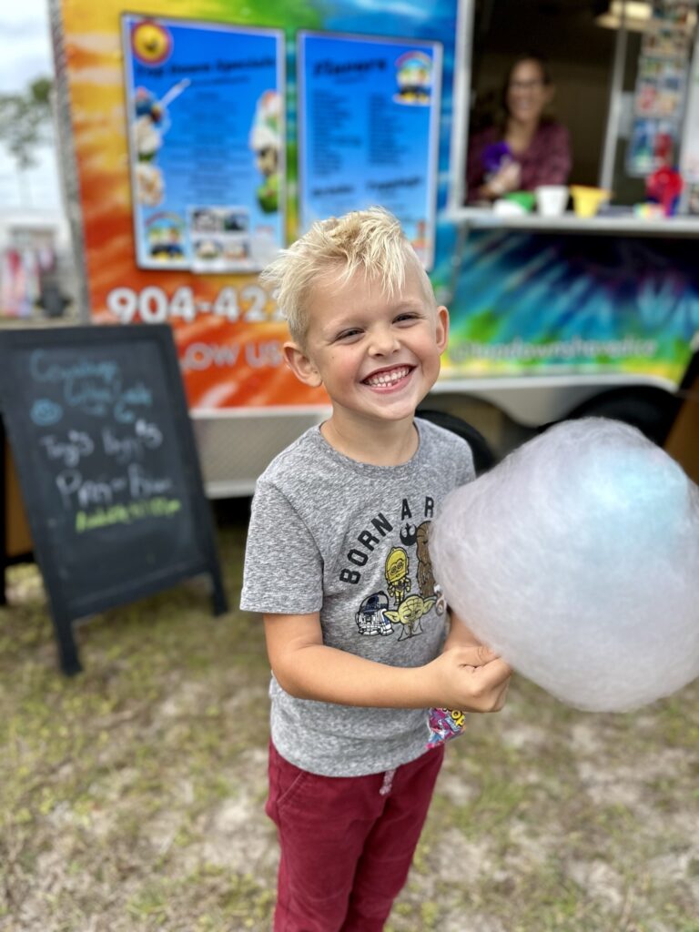 A little boy with a stick of pink cotton candy in front of the Top Down Shaved Ice truck.