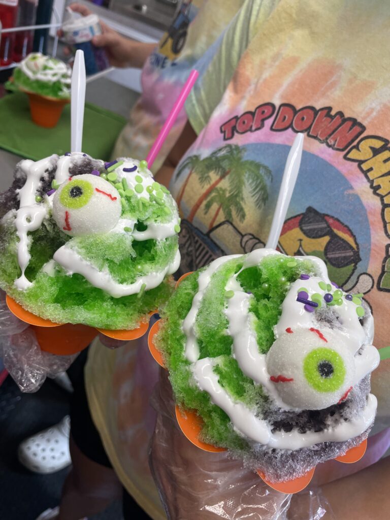 Two primarily green shaved ice with white flavoring and candy eyeballs.